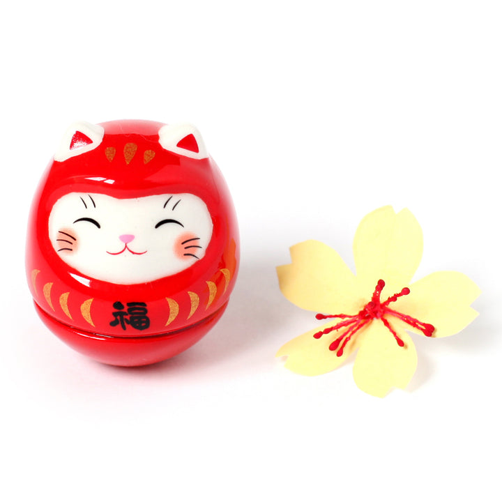 photo packshot d'un culbuto japonais (ou kororin) en céramique en forme de daruma chat rouge et d'une fleurs de cerisier jaune en papier japonais