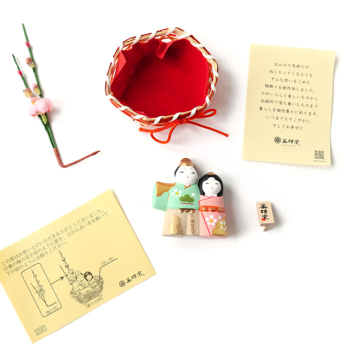 photo packshot d'un détail du packaging ducouple en céramique « hina matsuri » dans les tons vert d'eau, roses et dorés présenté dans son panier orné de fleurs de pêcher 