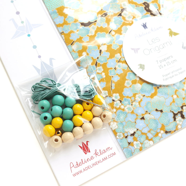 photo packshot d'un détail du packaging du kit guirlande de grues en origami dans les tons jaune moutarde, jaune caramel, vert d'eau, vert menthe et dorés de la gamme « pollen » (U9) adeline klam