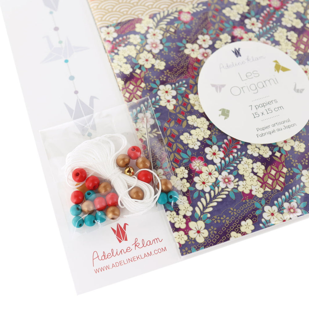 photo packshot dd'un détail du packaging du kit créatif guirlande de grues en origami « obachan » (J7) dans les tons violet foncé, noirs, rouge carmin et dorés adeline klam