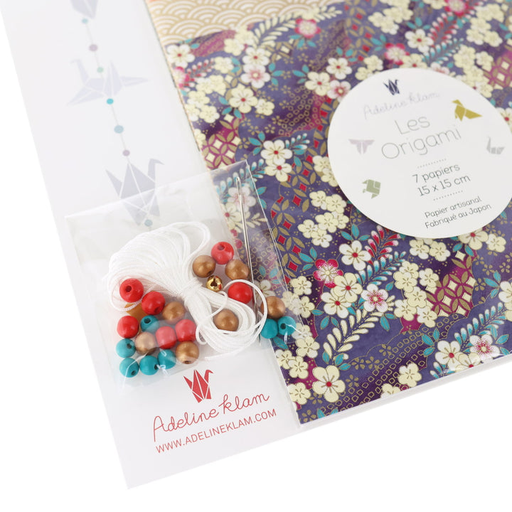 photo packshot dd'un détail du packaging du kit créatif guirlande de grues en origami « obachan » (J7) dans les tons violet foncé, noirs, rouge carmin et dorés adeline klam
