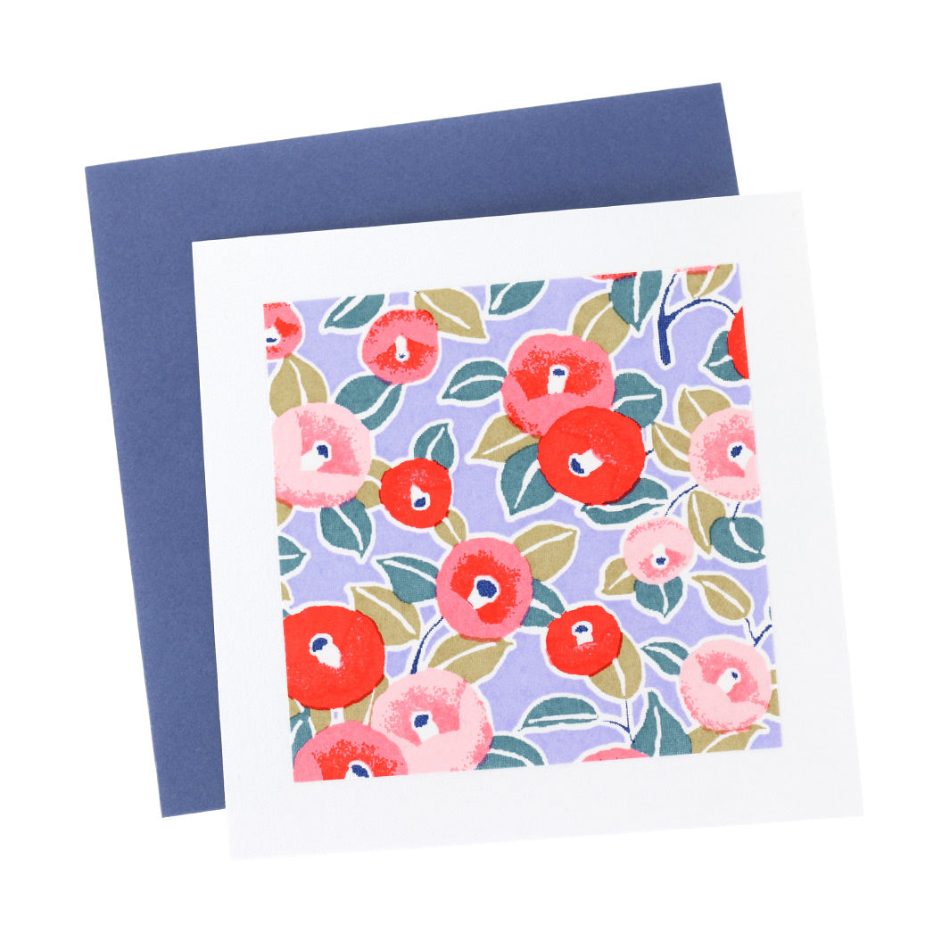 photo packshot vue de face de la carte carrée double habillée d'un carré de papier japonais de 13cm aux motifs de camélias dans les tons lavande, rouges et roses (M1012) et son enveloppe bleu foncé adeline klam