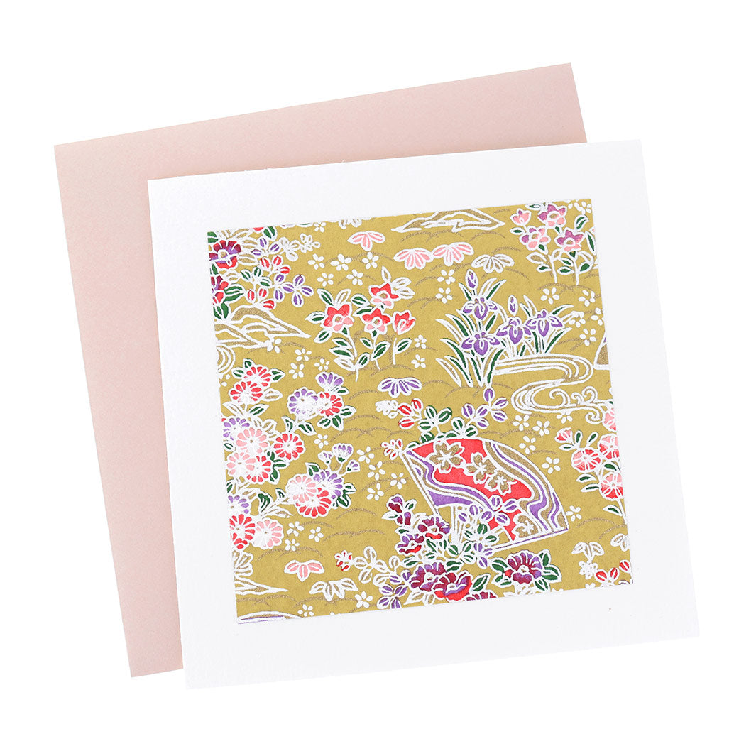 photo packshot vue de face de la carte carrée double habillée d'un carré de papier japonais de 13cm aux motifs d'éventails fleuris dans les tons jaune moutarde, roses, violets et vert foncé (M1048) et son enveloppe rose clair adeline klam