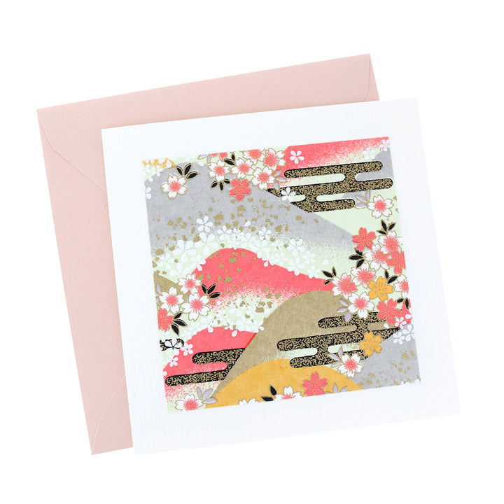 photo packshot vue de face de la carte carrée double habillée d'un carré de papier japonais de 13cm au motifs de montagnes et de fleurs de cerisier dans les tons roses, jaunes, verts, gris et doré (M1033) et son enveloppe rose clair adeline klam
