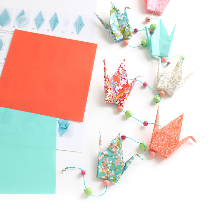 photo packshot de la guirlande montée et de l'intérieur du livret explicatif du kit créatif guirlande de grues en origami « floraison » (K10) dans les tons vert menthe, roses, corail et orange adeline klam