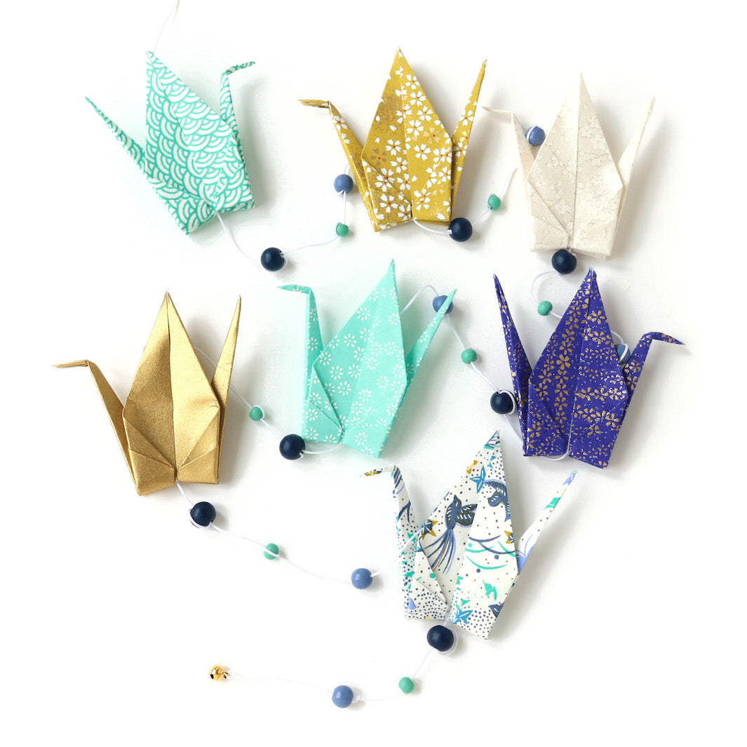 photo packshot de la guirlande montée du kit créatif guirlande de grues en origami « réglisse » (Z12) dans les tons vert d'eau, jaune moutarde, blanc cassé et bleu nuit adeline klam