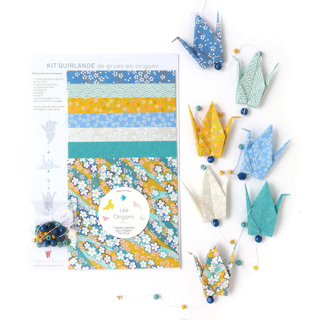 photo packshot de la guirlande montée et du packaging du kit créatif guirlande de grues en origami « vahiné » (U6) dans les tons jaune moutarde, bleu pervanche et canard et vert d'eau adeline klam