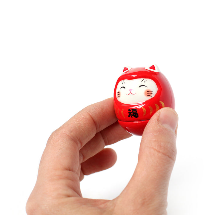 photo packshot dans une main d'un culbuto japonais (ou kororin) en céramique en forme de daruma chat rouge