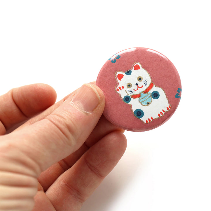 photo packshot en main du recto de l'aimant en papier japonais de 45mm de diamètre aux motifs de maneki-neko blancs aux détails rouges, bleu ciel et pétrole sur fond rouge lie de vin (M844) adeline klam