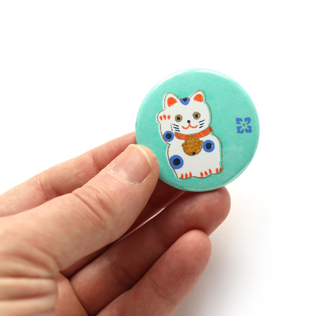 photo packshot en main du recto de l'aimant en papier japonais de 45mm de diamètre aux motifs de maneki-neko blancs aux détails corail et bleu violet sur fond vert menthe (M838) adeline klam