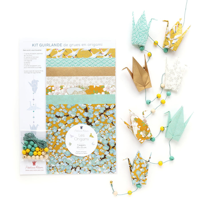photo packshot du packaging et de la guirlande montée du kit guirlande de grues en origami dans les tons jaune moutarde, jaune caramel, vert d'eau, vert menthe et dorés de la gamme « pollen » (U9) adeline klam