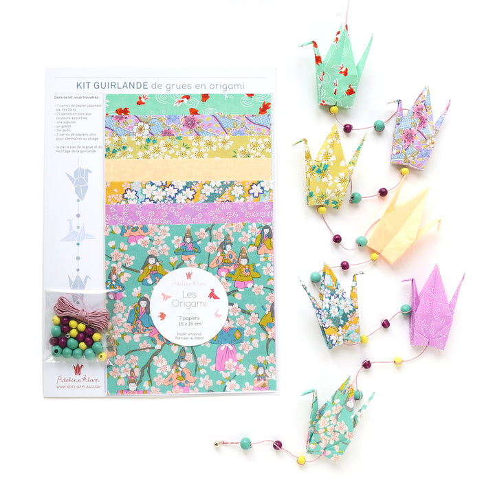 photo packshot du packaging et de la guirlande montée du kit guirlande de grues en origami dans les tons vert d'eau, vert menthe, jaune moutarde et orange pastel de la gamme « confiserie » (K12) adeline klam