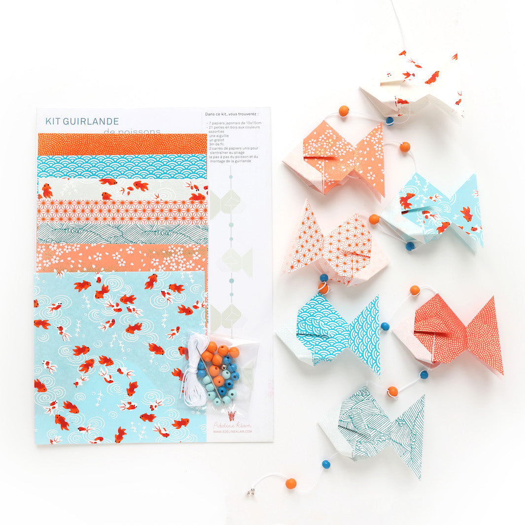 photo packshot du packaging et de la guirlande montée du kit guirlande de poissons en origami dans les tons bleu ciel, turquoise, corail, rouges et oranges de la gamme « sunset » adeline klam