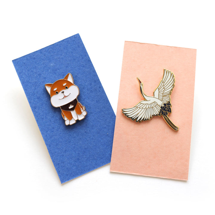 photo packshot des pin's en forme de shiba inu roux et blanc et de grue en vol blanche