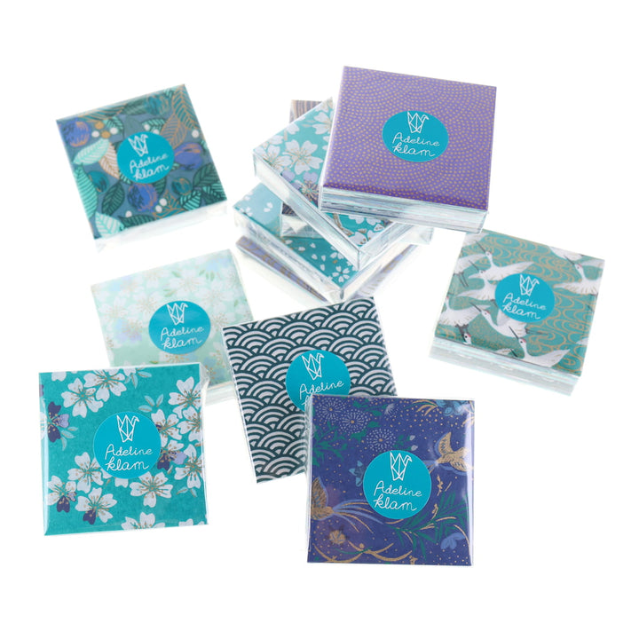 photo packshot de sets de 100 carrés de papiers japonais adeline klam de 6cm par 6cm dans les tons bleu canard, vert d'eau, bleu nuit, turquoise et violets « paon »