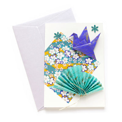 photo packshot en vue du dessus de la carte double habillée d'un carré de papier japonais et d'origami de grue et d'éventail dans les tons bleu turquoise, vert d'eau, jaune moutarde et violets