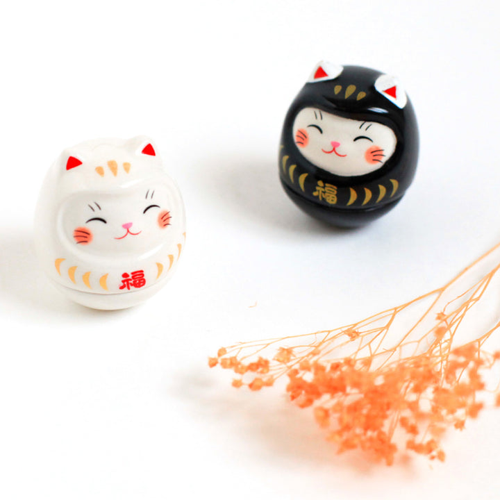 petits culbutos japonais ou koro-rin en forme de daruma chat blanc et noir de face et fleurs séchées orange