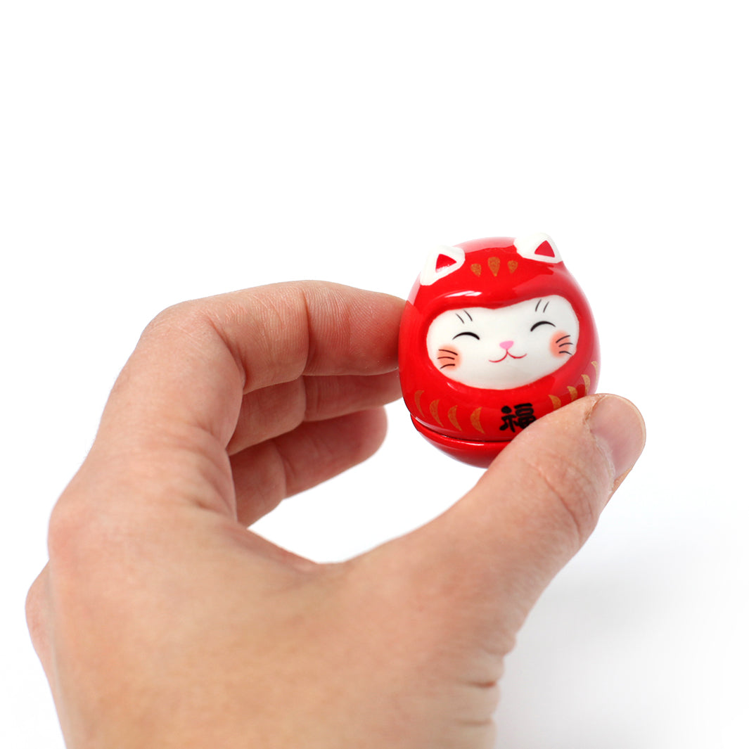 petit culbuto japonais ou koro-rin en forme de daruma chat rouge de face dans une main