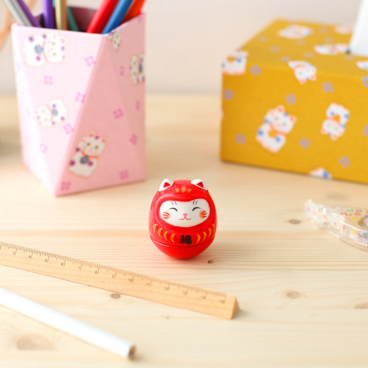 petit culbuto japonais ou koro-rin en forme de daruma chat rouge sur un bureau